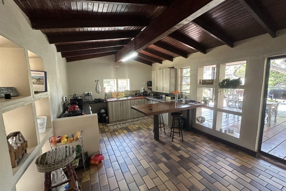 Spacious kitchen featuring exposed timber beam ceilings, tiled flooring, built-in cabinetry, and a central island, with large windows providing natural light and garden views.