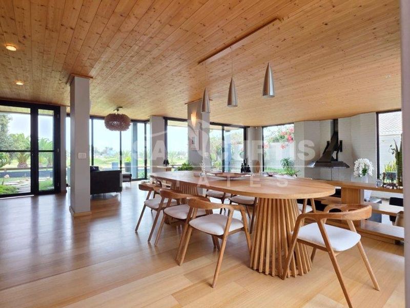 Spacious open-plan living and dining area featuring warm timber ceilings, hardwood flooring, a unique suspended fireplace, and expansive floor-to-ceiling glass doors.