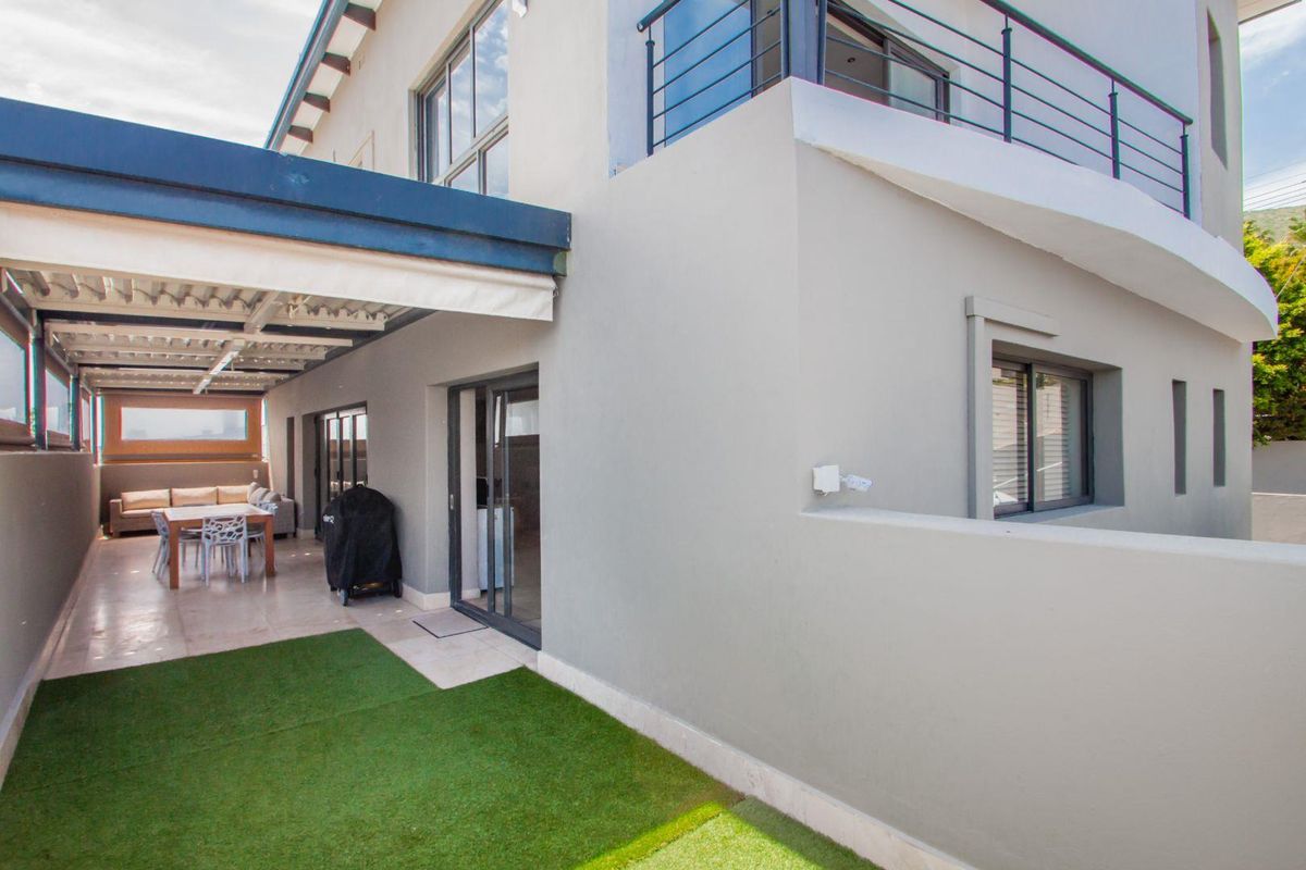 A well-maintained rear exterior featuring a covered patio area, artificial lawn, and an upper-level balcony with metal railings.
