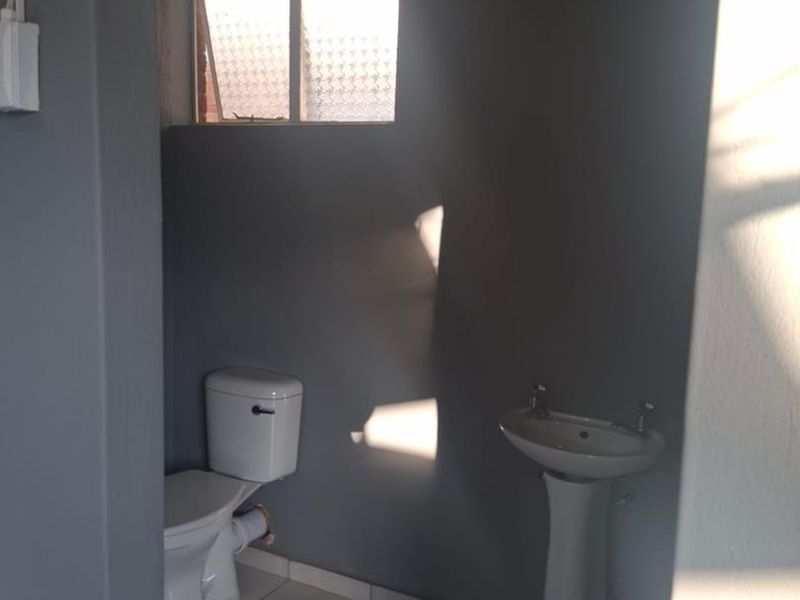 A compact bathroom featuring a pedestal basin, toilet, and tiled flooring, finished in a neutral grey tone.