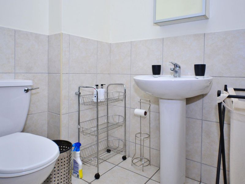 A functional bathroom featuring a pedestal basin, toilet, and neutral wall and floor tiling.