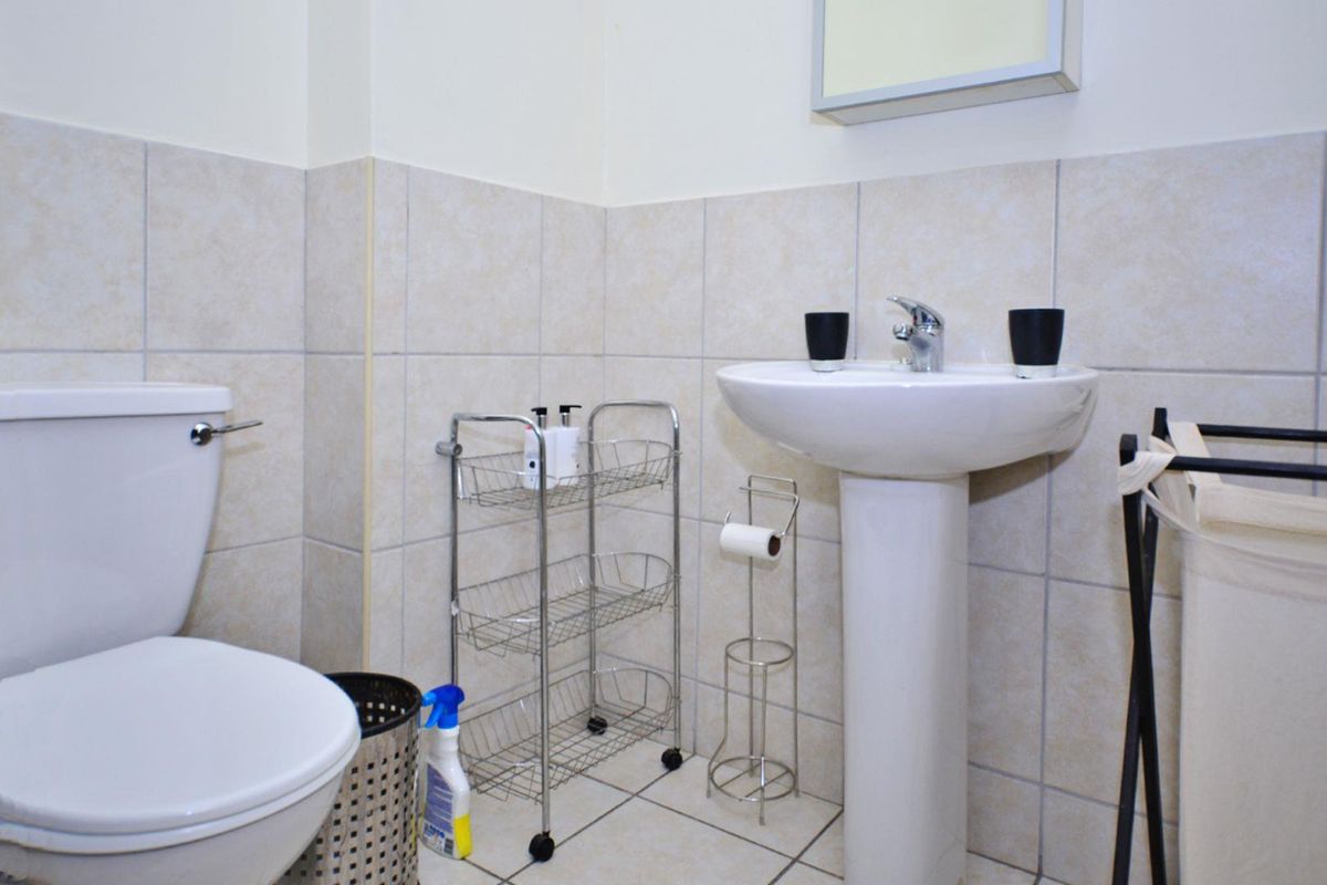 A functional bathroom featuring a pedestal basin, toilet, and neutral wall and floor tiling.