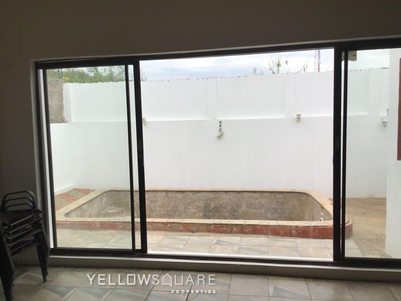 View of a backyard pool area featuring a concrete pool shell, tiled patio, and perimeter boundary wall, accessible via large sliding glass doors.