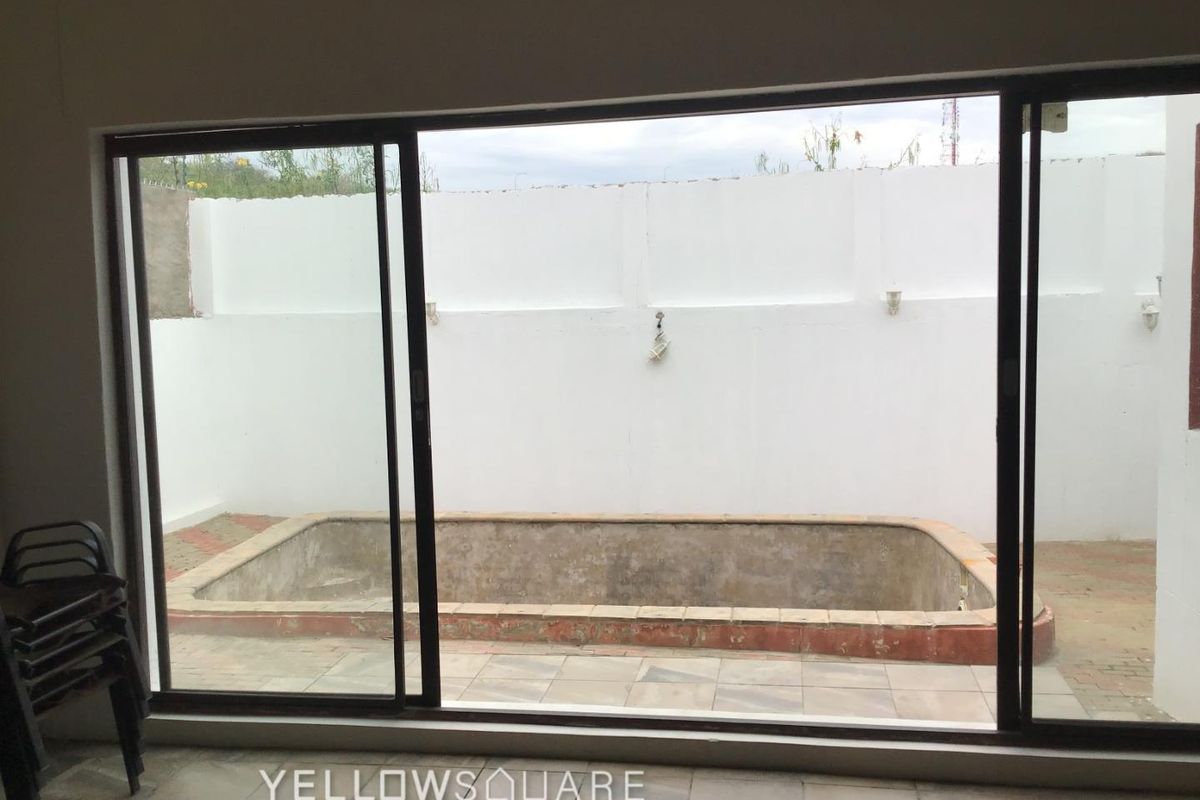 View of a backyard pool area featuring a concrete pool shell, tiled patio, and perimeter boundary wall, accessible via large sliding glass doors.