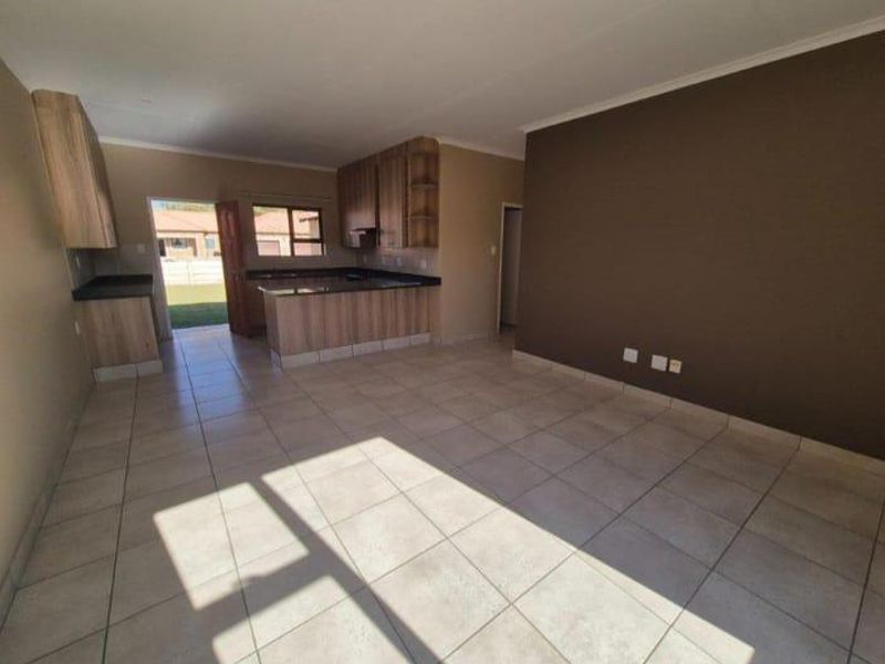 Open-plan living area featuring tiled flooring and a functional kitchen with built-in cabinetry and laminate countertops, leading to an exterior entrance.