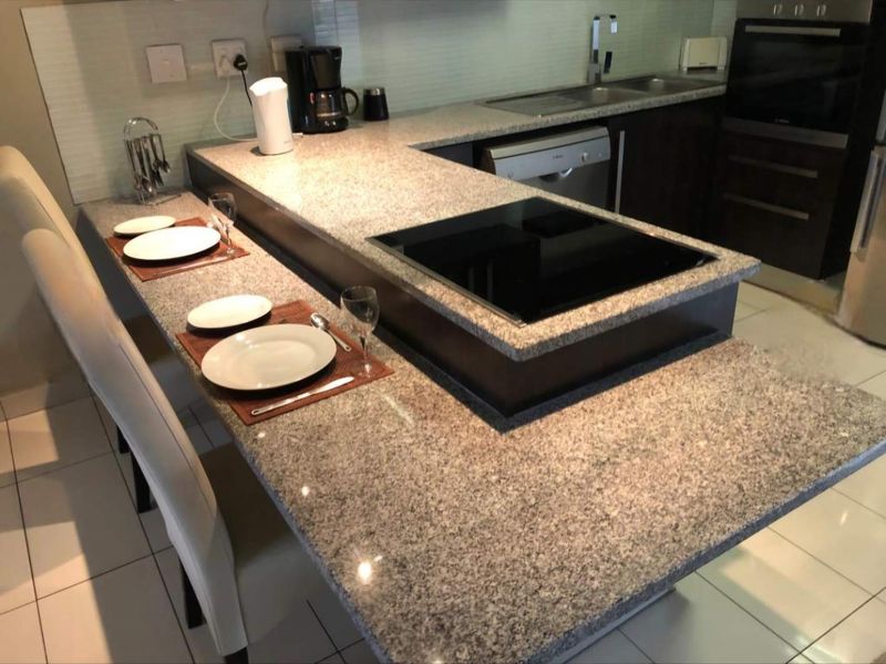 Modern kitchen featuring granite countertops, a built-in hob, integrated dishwasher, and sleek cabinetry with tiled flooring throughout.