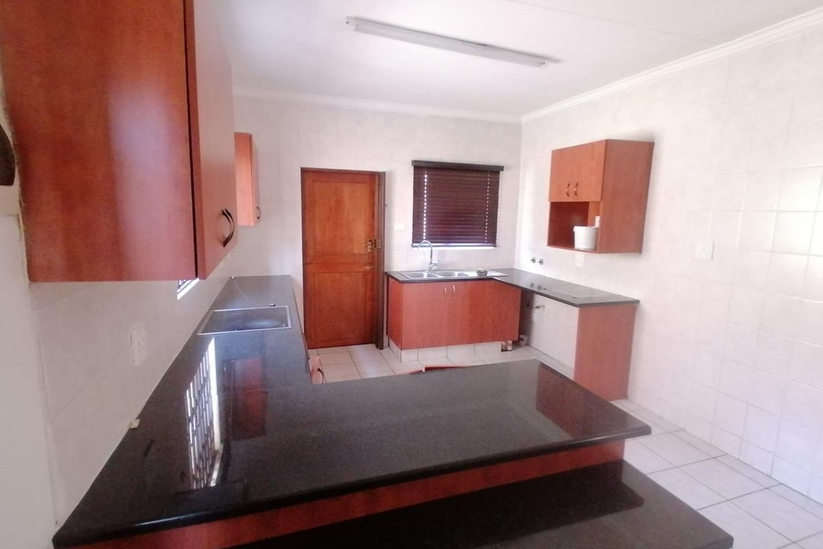 A functional kitchen featuring dark granite countertops, wood-finish cabinetry, tiled splashbacks, and tiled flooring, offering a clean and practical workspace.