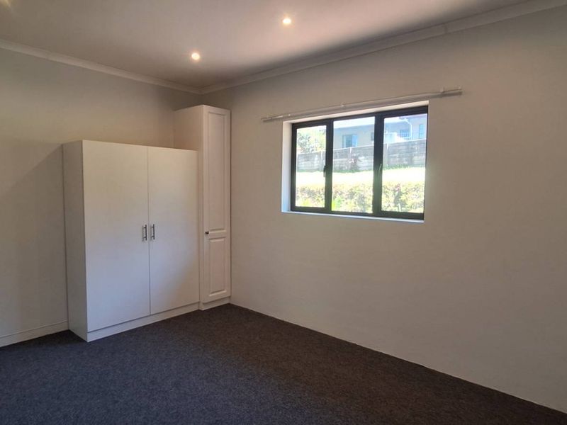 A clean, empty bedroom featuring neutral walls, dark carpeting, recessed downlighting, and built-in storage cupboards.