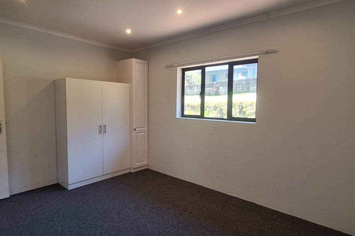 A clean, empty bedroom featuring neutral walls, dark carpeting, recessed downlighting, and built-in storage cupboards.