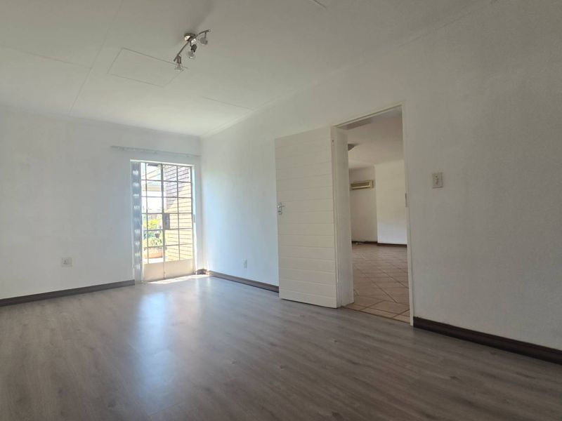 A bright, empty living room featuring modern laminate flooring, a glass panel door leading outside, and neutral white walls.