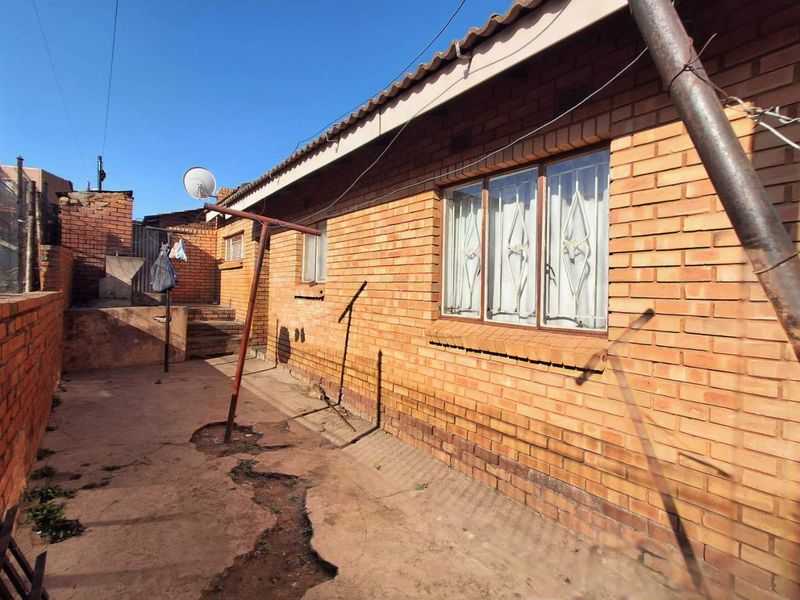Rear exterior view of a face brick house featuring a tiled roof and a paved backyard area with visible signs of wear.