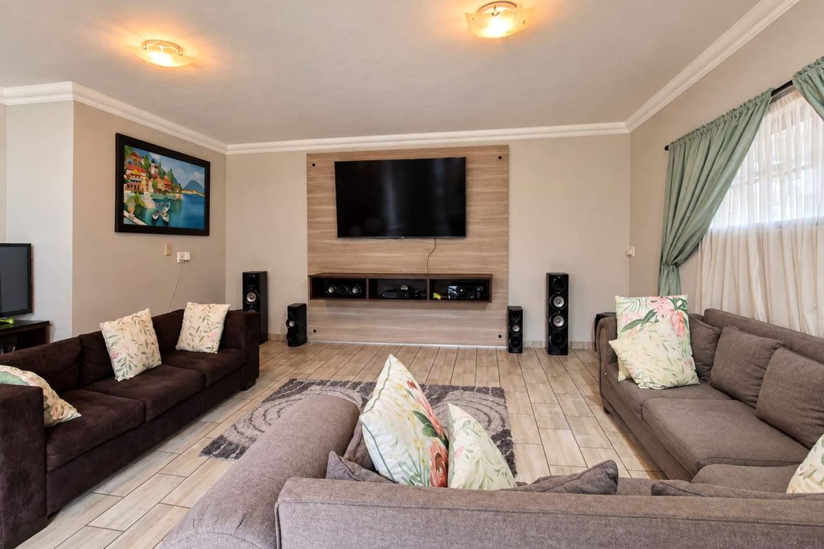 A well-maintained living room featuring tiled flooring, a modern built-in media wall unit, and decorative cove cornicing.