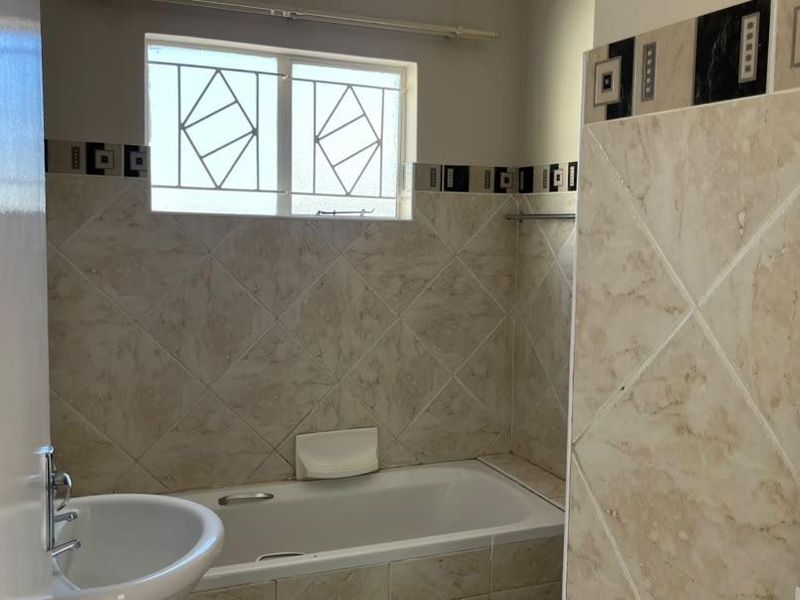 A functional bathroom featuring a bathtub, pedestal basin, and neutral tiled walls with decorative border accents.