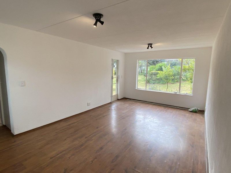 A bright, empty living room featuring laminate flooring, an arched entryway, and large windows overlooking the garden.