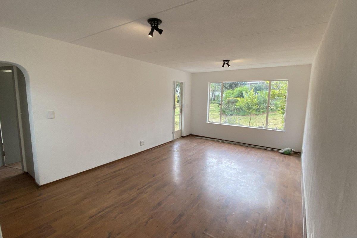 A bright, empty living room featuring laminate flooring, an arched entryway, and large windows overlooking the garden.