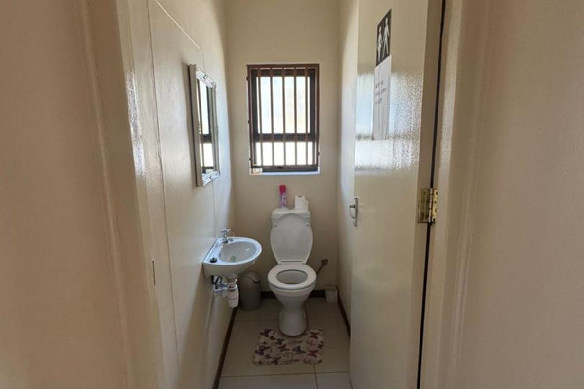 A compact office restroom featuring a wall-mounted basin, toilet, and tiled flooring with a small window for ventilation.
