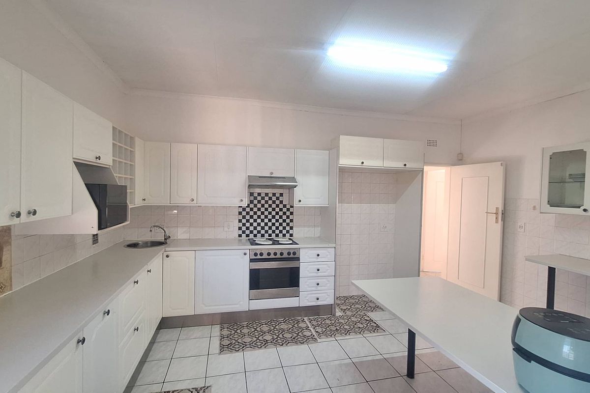 A functional kitchen featuring white cabinetry, a built-in oven with extractor fan, tiled splashbacks, and a convenient breakfast bar area.