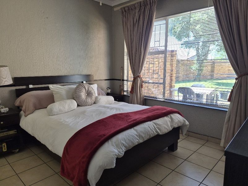 A bedroom featuring tiled flooring and a large window with venetian blinds, offering natural light and a view of the outdoor area.