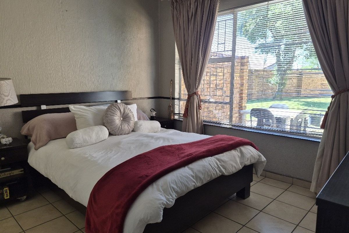 A bedroom featuring tiled flooring and a large window with venetian blinds, offering natural light and a view of the outdoor area.