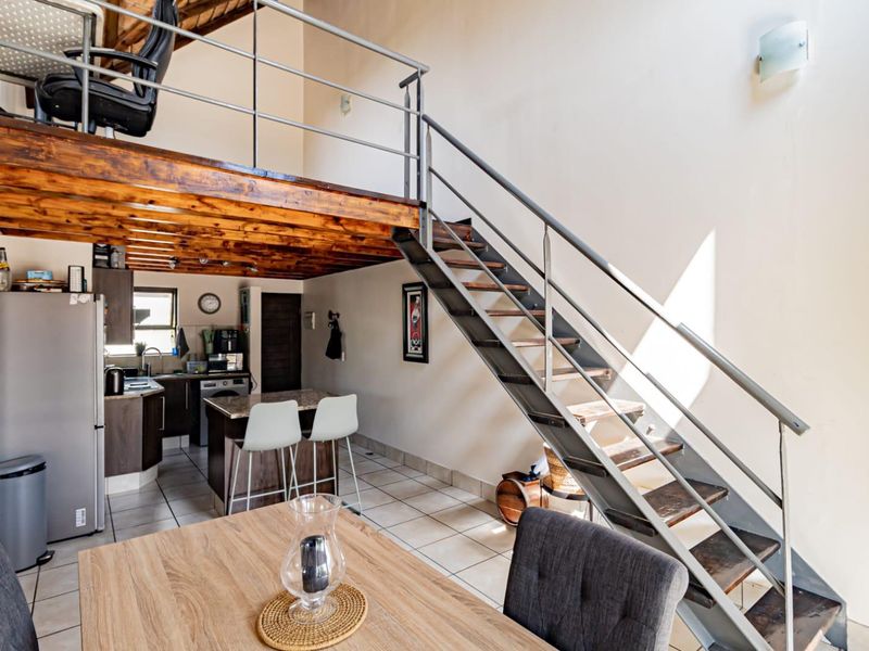 Open-plan living area featuring a mezzanine level, metal staircase, tiled flooring, and a functional kitchen with an island.