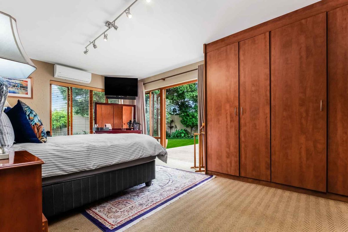 Spacious bedroom featuring built-in wooden cabinetry, split-system air conditioning, and large glass doors opening onto a private garden area.