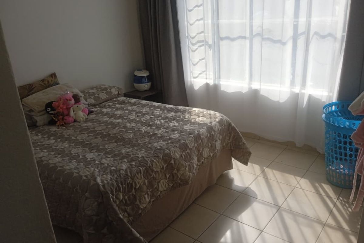 A functional bedroom featuring tiled flooring and large windows with curtain tracks, providing natural light to the space.