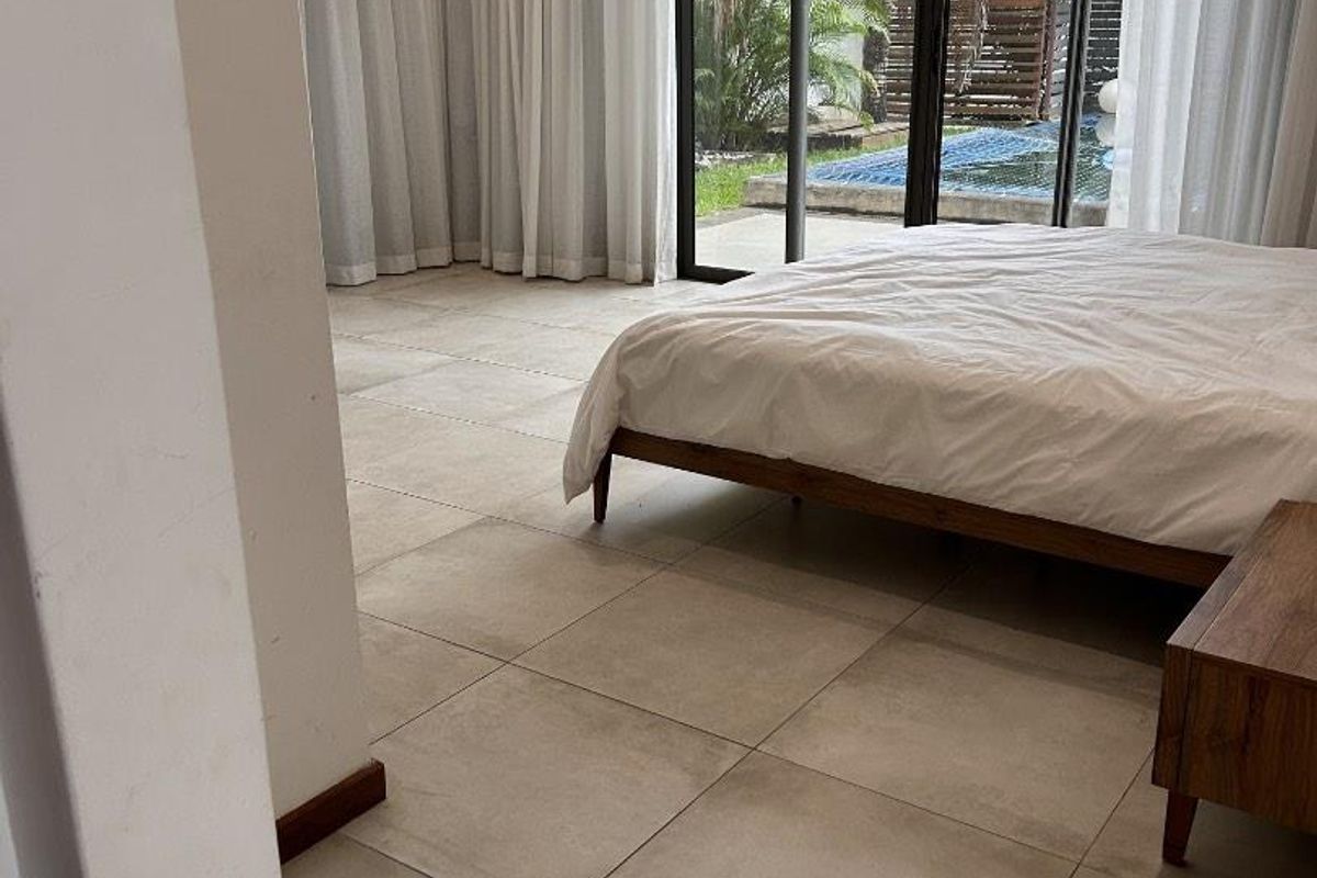 Spacious bedroom featuring large format floor tiles, floor-to-ceiling curtains, and sliding glass doors providing direct access to the outdoor pool area.