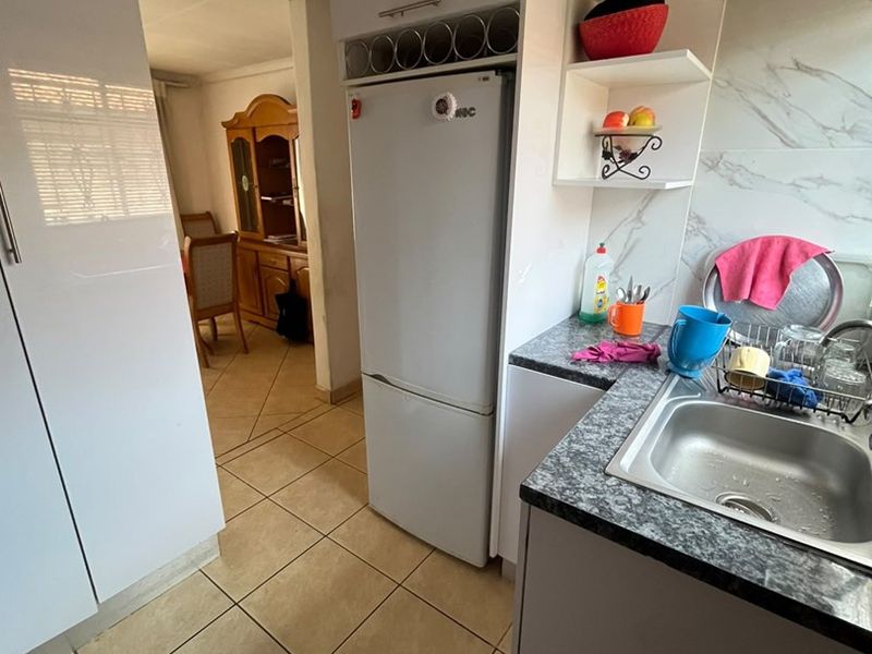 A functional kitchen featuring white built-in cabinetry, granite-look laminate countertops, a stainless steel sink, and tiled flooring, with an open flow to the dining area.
