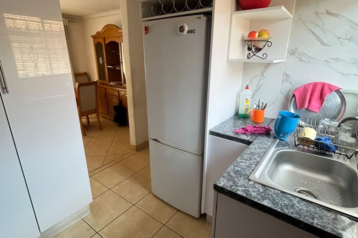 A functional kitchen featuring white built-in cabinetry, granite-look laminate countertops, a stainless steel sink, and tiled flooring, with an open flow to the dining area.