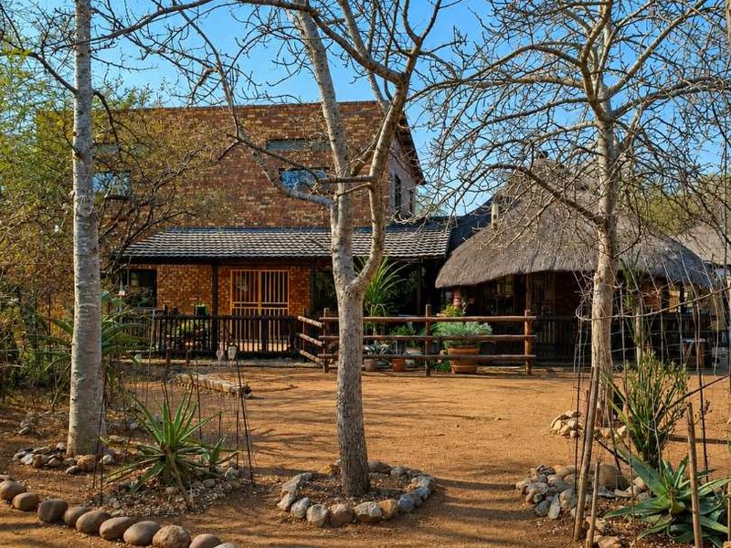 A view of the rear exterior featuring a brick building with a thatched roof section, timber fencing, and a natural landscaped garden area.