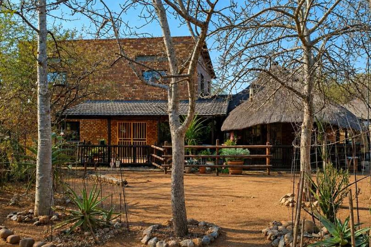 A view of the rear exterior featuring a brick building with a thatched roof section, timber fencing, and a natural landscaped garden area.