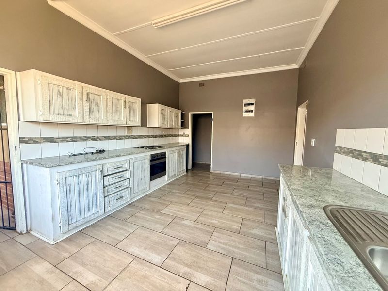 Spacious kitchen featuring granite countertops, built-in cabinetry, integrated oven and hob, and tiled flooring throughout.