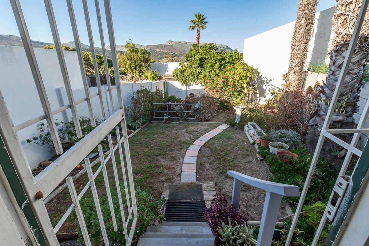 A private rear garden featuring a paved pathway, established greenery, and mountain views, accessed via a metal gate and concrete steps.