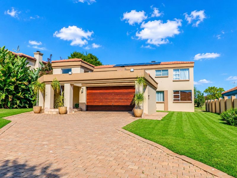 Front view of a well-maintained residential property featuring a paved driveway, double garage, and solar panels on a tiled roof.