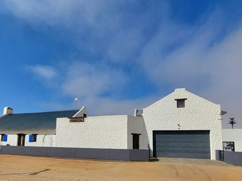 A well-maintained house featuring a textured white facade, metal roofing, and a secure garage, set behind a modern boundary wall.