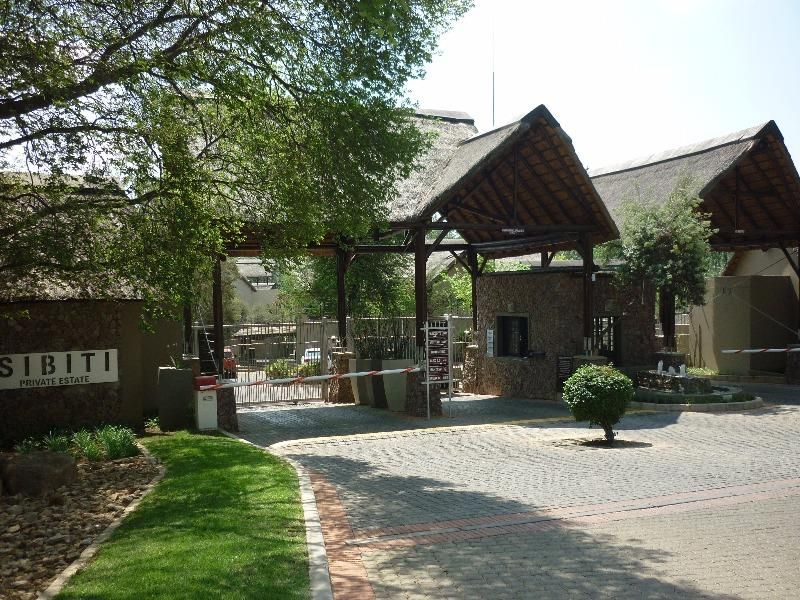 The entrance to Sibiti Private Estate featuring a thatched roof security gatehouse, stone masonry, and a paved driveway with controlled access.