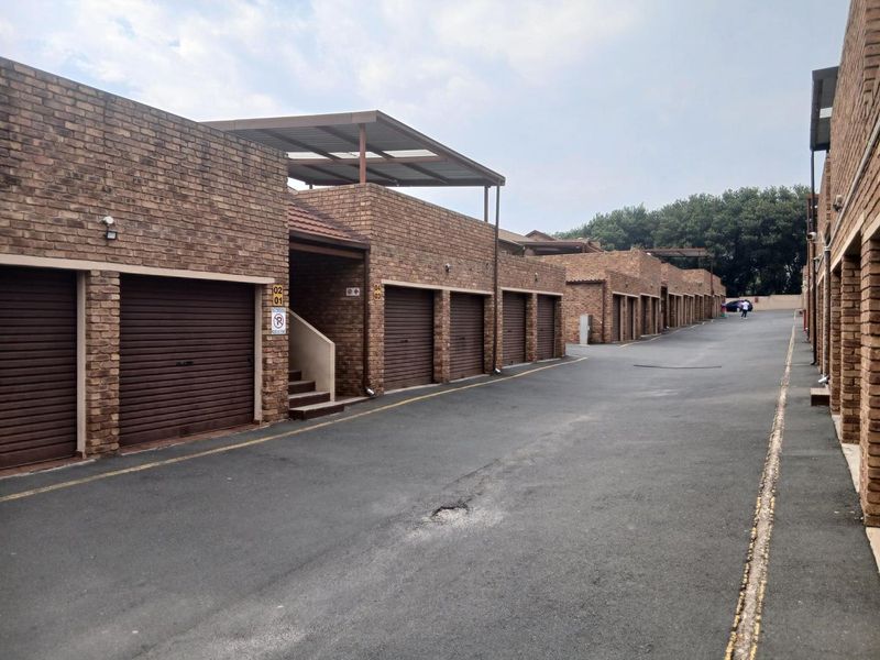 A row of brick-faced garages with roller shutter doors and an asphalt driveway in a townhouse complex.