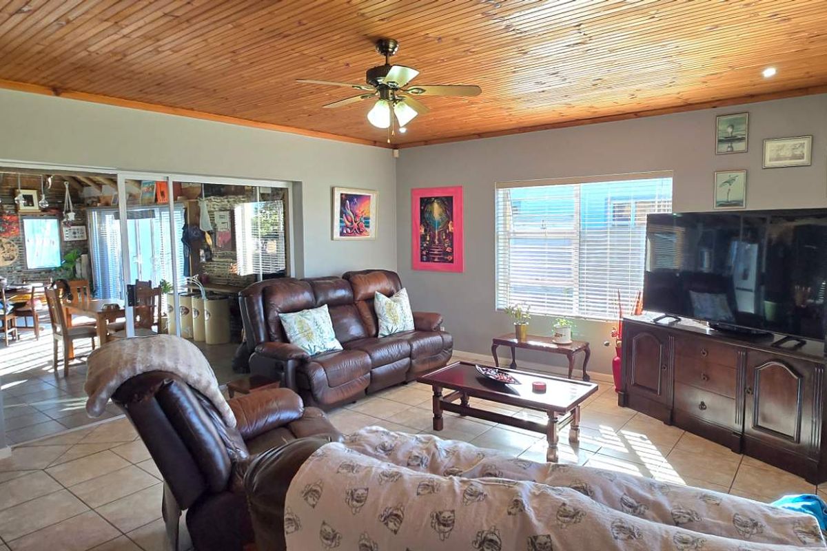Spacious living room featuring a timber-clad ceiling, tiled flooring, and large windows, with an open-plan flow leading into the adjacent dining area.