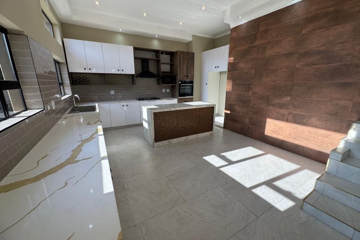 Modern kitchen featuring marble-look quartz countertops, a central island, built-in oven, gas hob, and stylish feature wall tiling with recessed ceiling lighting.