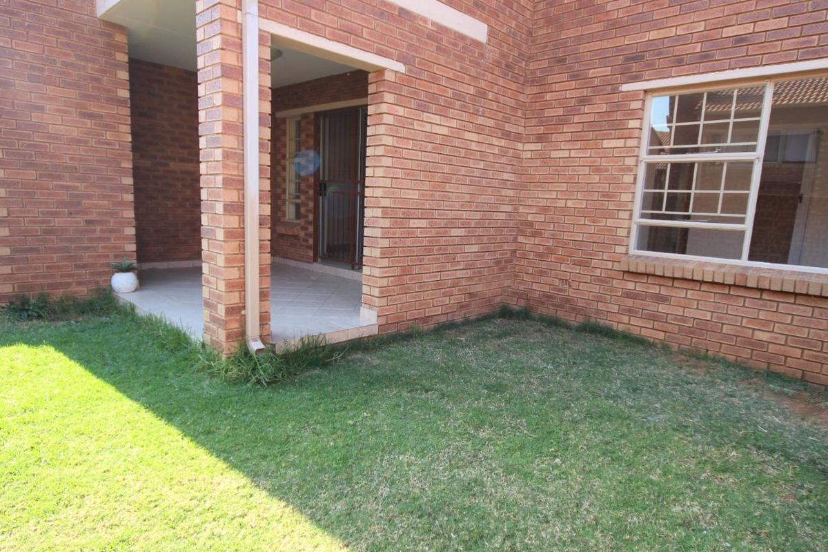 Rear view of the apartment featuring a covered patio area, brick exterior walls, and a small private garden space.