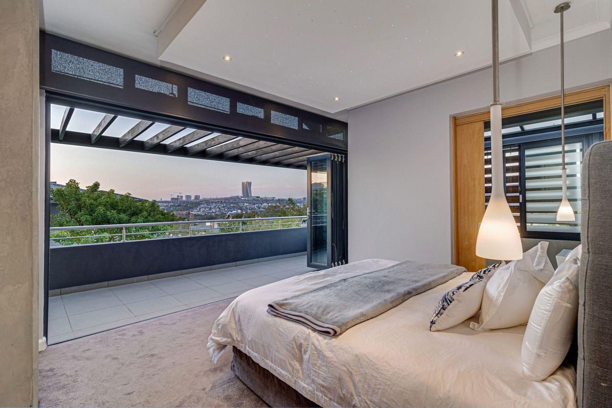 Spacious bedroom featuring a recessed ceiling with integrated fiber optic lighting and large bi-fold doors opening onto a private balcony with city views.