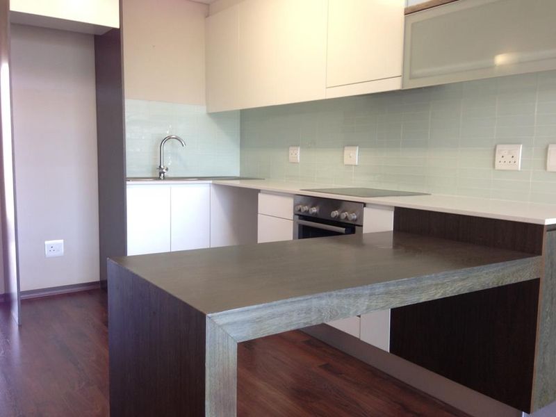 Modern kitchen featuring white cabinetry, stone countertops, glass splashback, integrated oven, and a dark wood-look breakfast bar island.