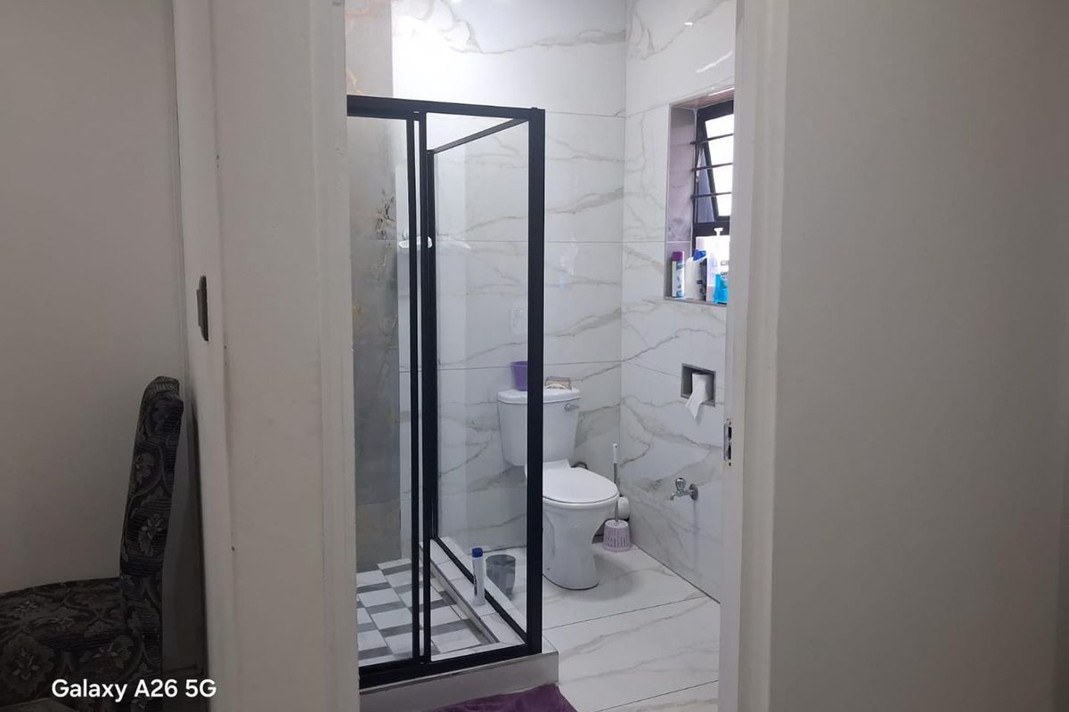 A modern bathroom featuring a glass-enclosed shower, white toilet, and elegant marble-look wall tiling.