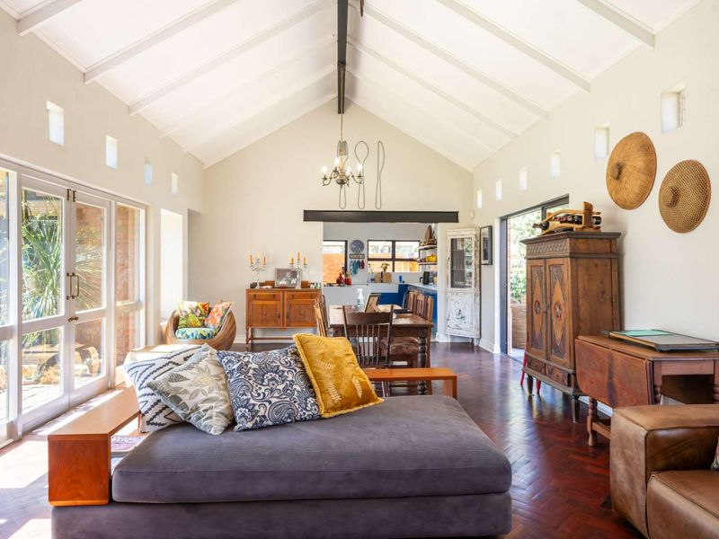 Spacious open-plan living and dining area featuring a high vaulted ceiling with exposed beams, herringbone parquet flooring, and large glass doors opening to the garden.