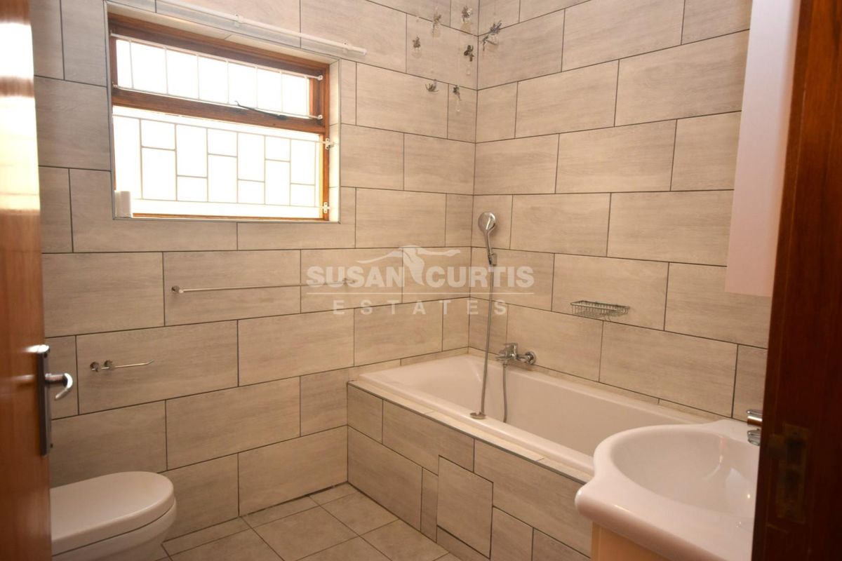 A clean, tiled bathroom featuring a built-in bathtub with shower attachment, pedestal basin, and toilet, finished with neutral wall and floor tiles.