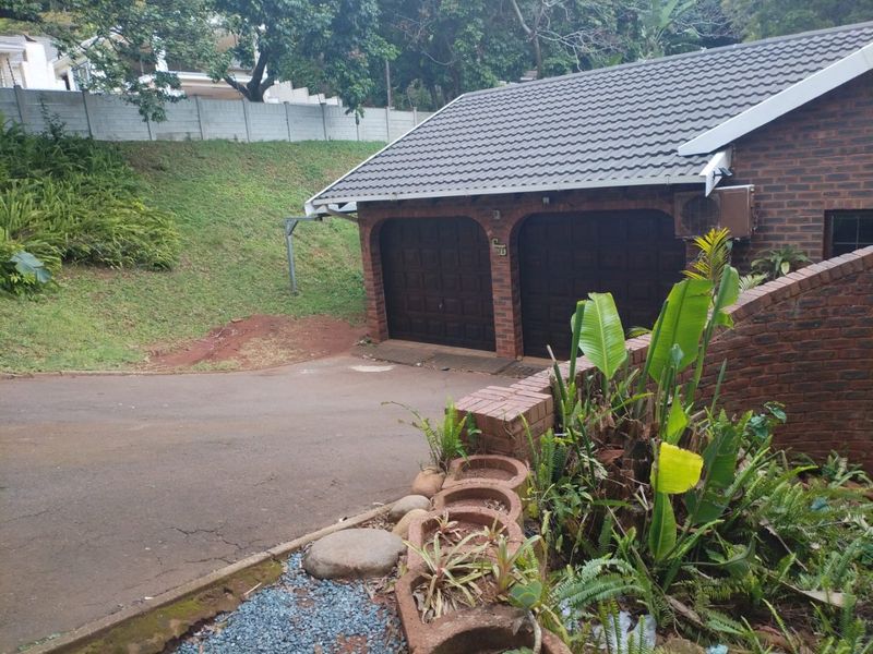 A double garage with brick exterior and tiled roof, featuring a paved driveway and landscaped retaining wall.