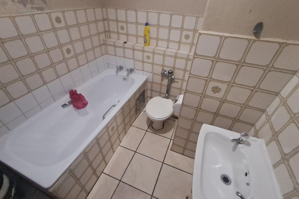 A dated bathroom featuring a standard bathtub, toilet, and pedestal basin with original wall and floor tiling.