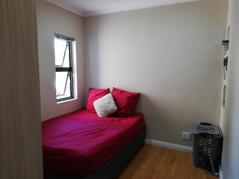 A compact bedroom featuring laminate flooring, a built-in cupboard, and a casement window, providing a functional and well-lit sleeping space.