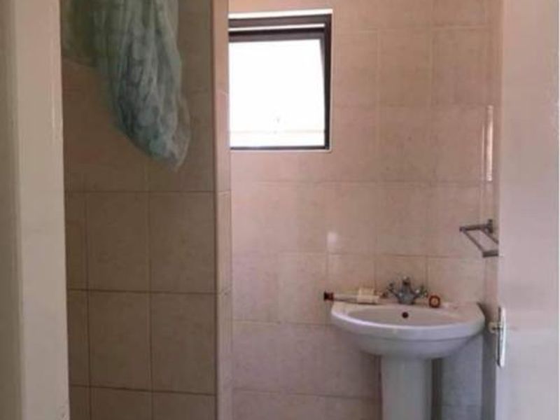A functional bathroom featuring a pedestal basin, tiled walls and flooring, and a dedicated shower partition wall with an awning window for ventilation.