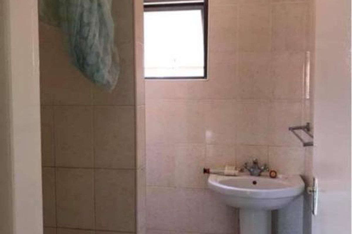 A functional bathroom featuring a pedestal basin, tiled walls and flooring, and a dedicated shower partition wall with an awning window for ventilation.